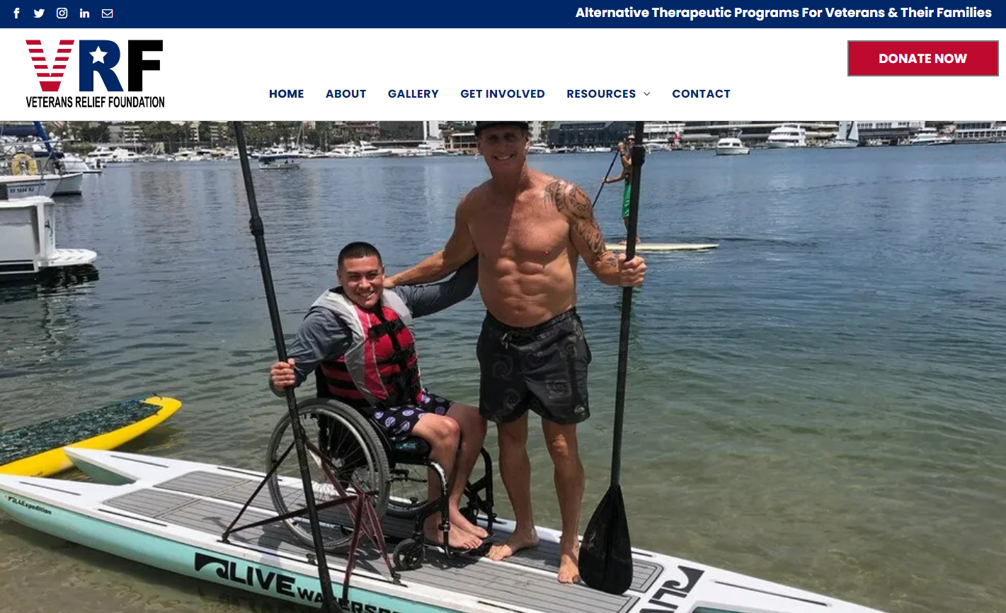 Man in wheelchair and shirtless man paddleboarding on water.