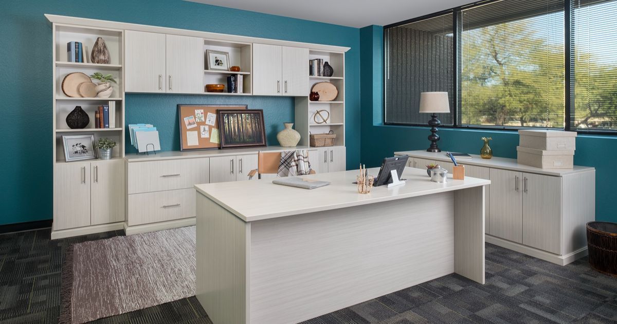 White office furniture in a teal-walled room with a large window. A desk, storage cabinets, and shelving are included.