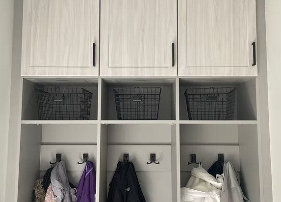 Mudroom storage with grey cabinets, baskets, hooks, and jackets.
