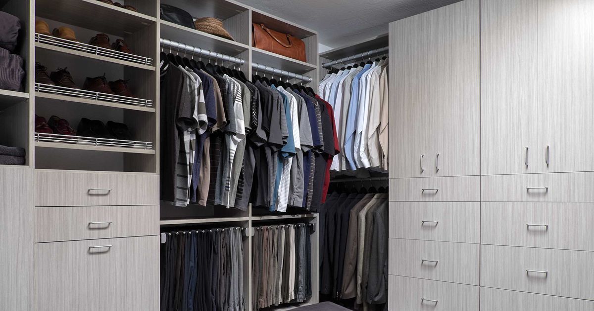 Walk-in closet with light-colored shelving, drawers, and hanging clothes: shirts, pants, and shoes.