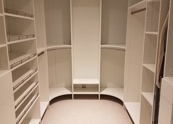 Empty white walk-in closet with shelves, hanging rods, and curved corner design.
