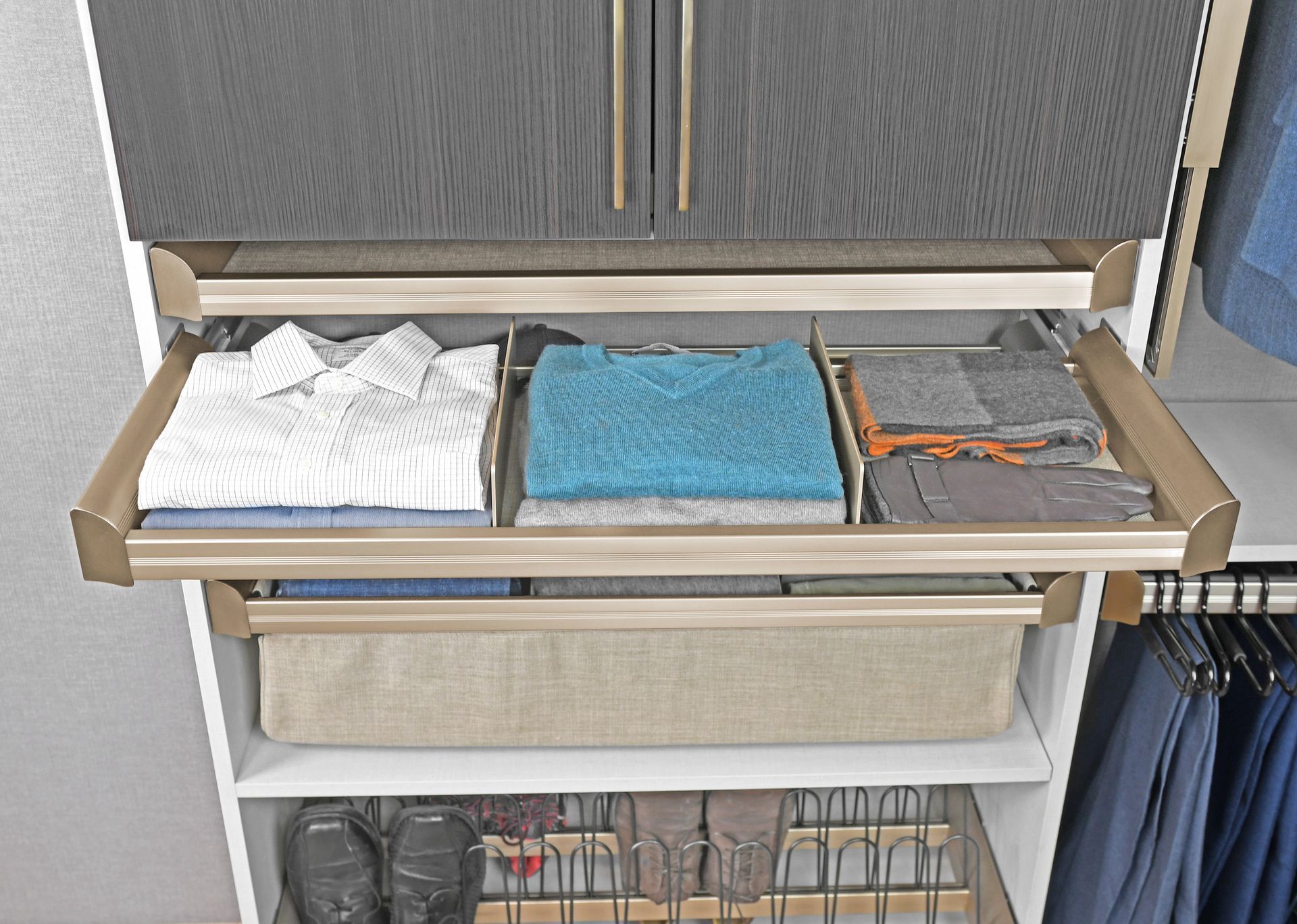 Closet with pull-out tray containing folded clothes. Beige drawer below with organizer. Gray cabinets above.