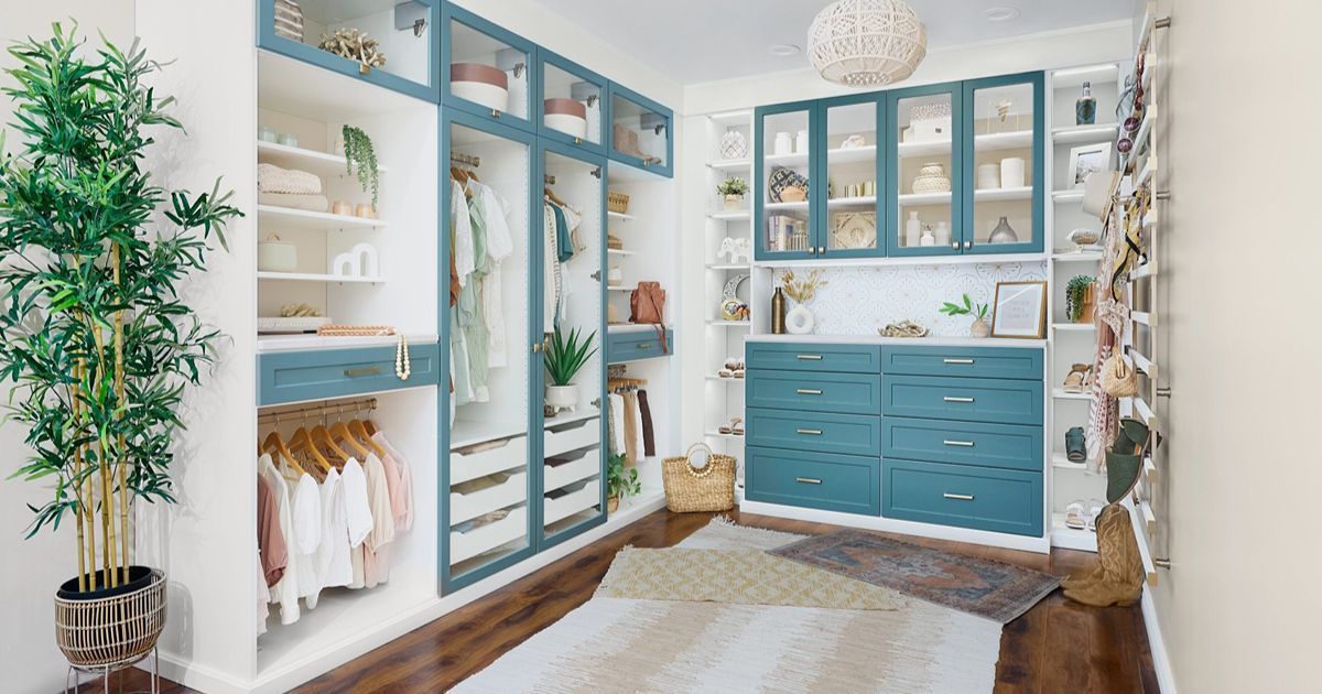 A walk-in closet with teal and white built-ins, housing clothes, shelves, and drawers. A large plant and rug are also visible.