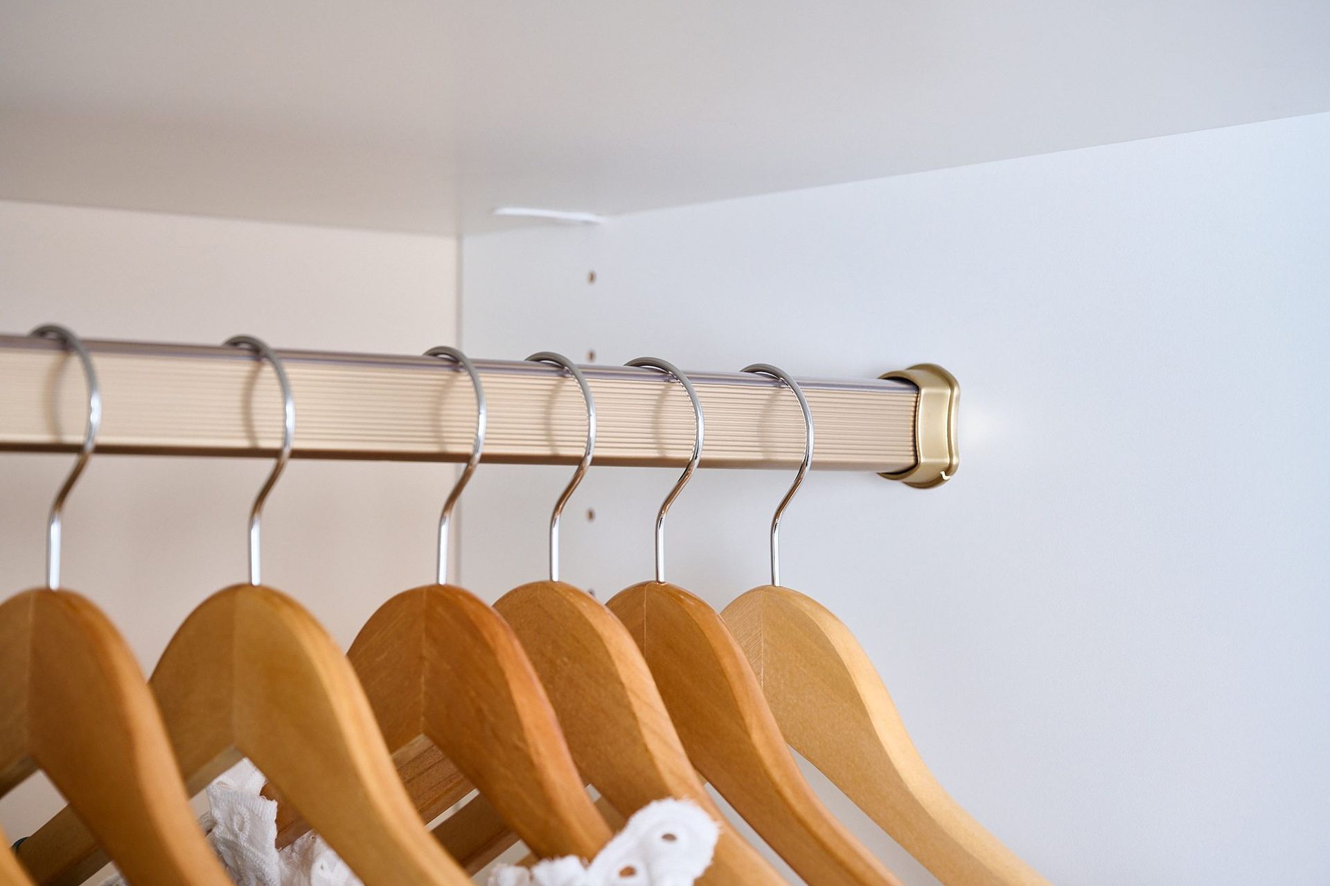 Wooden hangers in a white closet, hanging from a wooden rod, mostly empty.