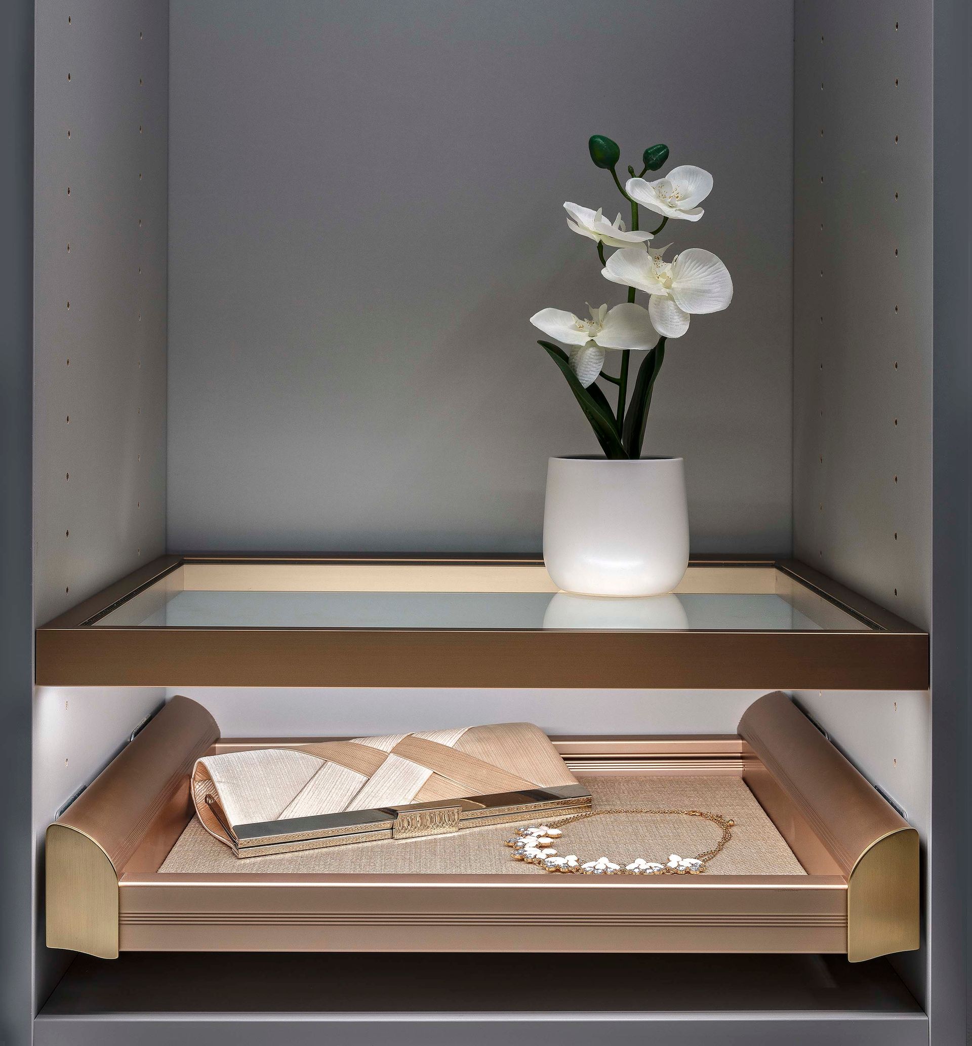 A lit shelf in a cabinet displays a white floral arrangement and rolled towels.