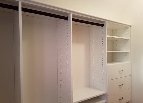 White closet with hanging rods, shelves, and drawers against a light-colored wall.