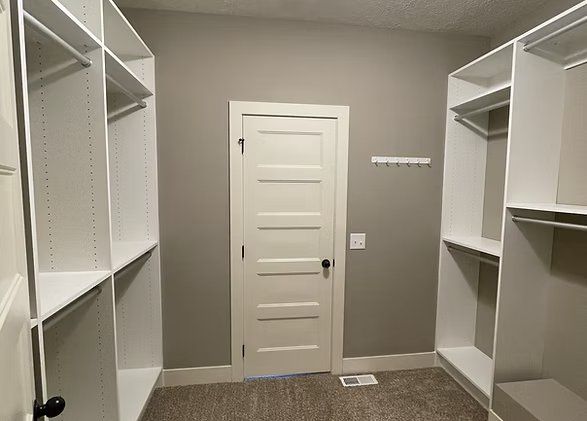 Walk-in closet with white shelves and a closed door. Gray walls, tan carpet.