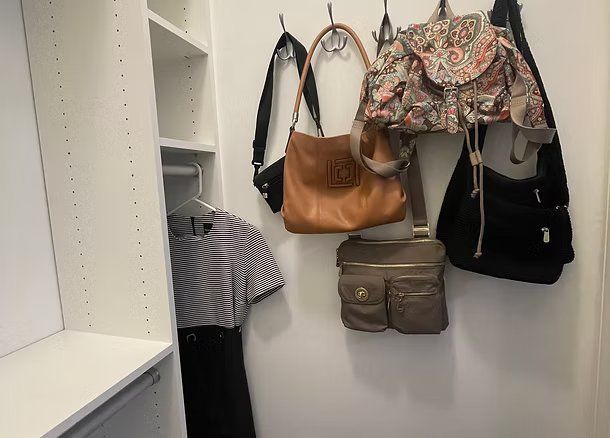 A walk-in closet with hanging purses on hooks and a dress.