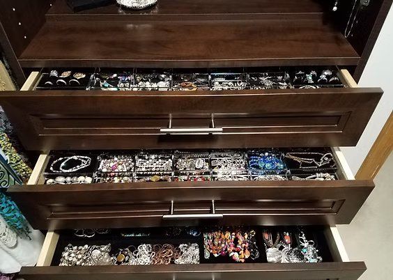 Three dark wood drawers filled with jewelry, including necklaces, bracelets, and rings.
