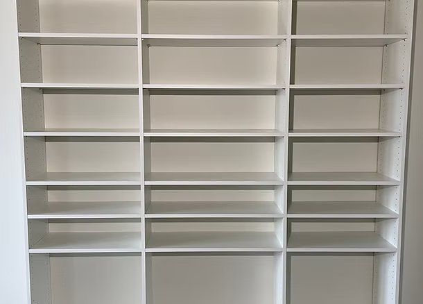 Empty white built-in shelves against a white wall. Three columns of various sized shelf spaces.