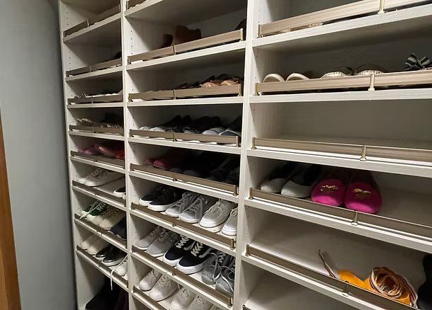 Shoe shelves filled with various shoes, in a closet with neutral walls.