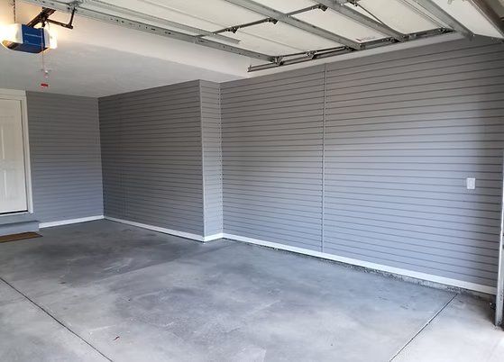 Empty garage with gray panel walls, concrete floor, and white trim.