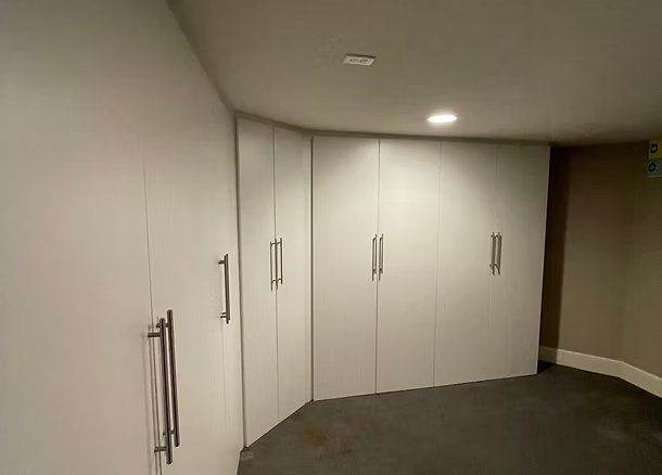 White built-in storage cabinets in a room with gray carpet and neutral walls.
