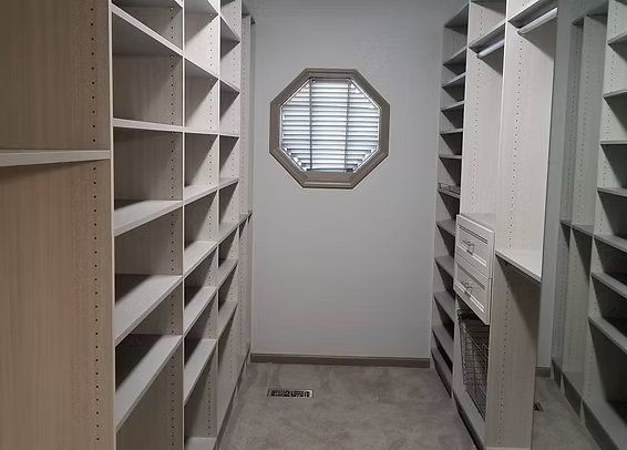 Empty walk-in closet with built-in shelving on both sides, a window at the end, and a gray carpet.