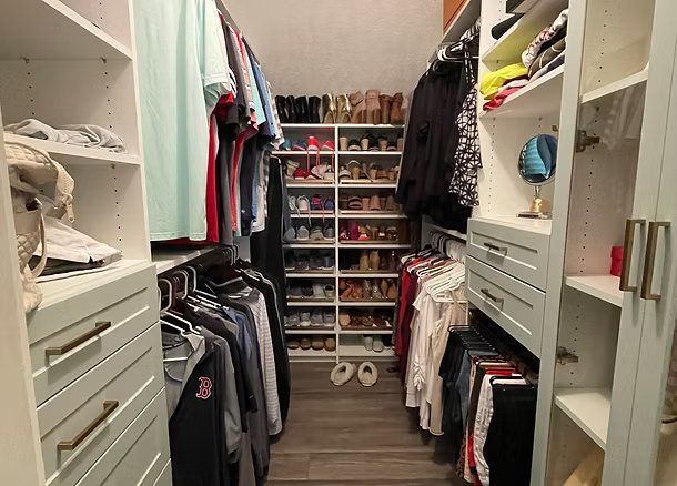 Walk-in closet with organized clothes, shoes, and shelves. White cabinetry with wood floor.