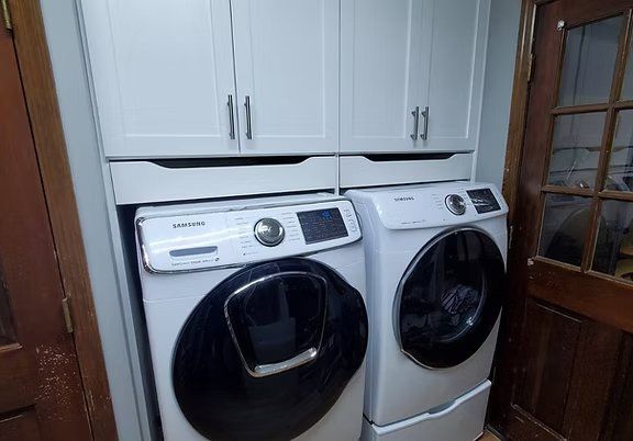White Samsung washer and dryer with upper cabinets in a laundry room.