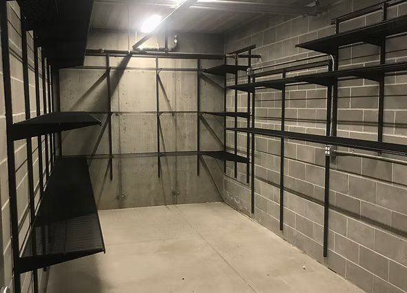 Empty storage room with gray cinder block walls and black metal shelving.