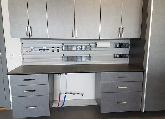 Gray workshop cabinets with drawers and workspace, pegboard with storage, and upper cabinets.