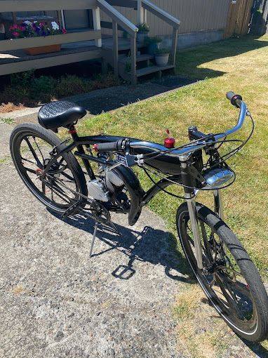 A black bicycle with a motor attached to it is parked on a sidewalk.