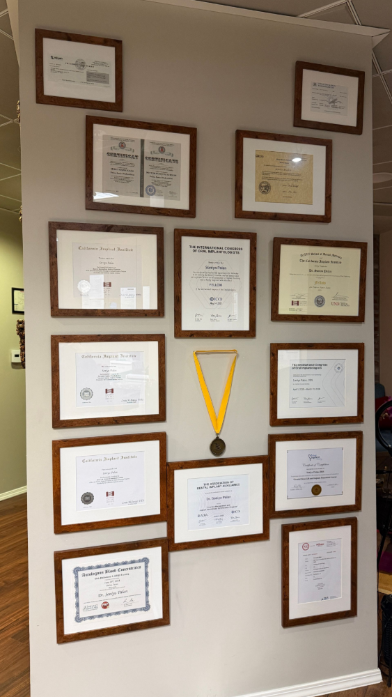 A wall gallery of framed certificates and awards, featuring a medal hanging from a yellow ribbon in the center.