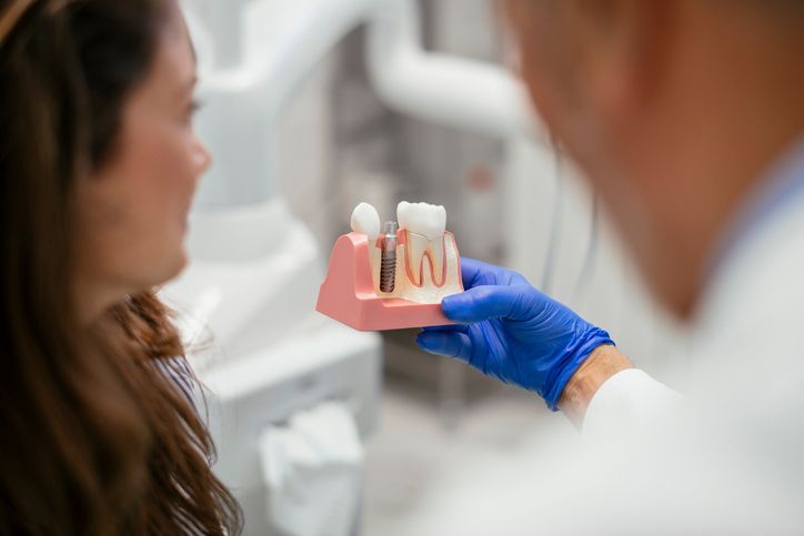 Dentist examining patient's teeth with shade guide in clinic. Two medical professionals, one patient.