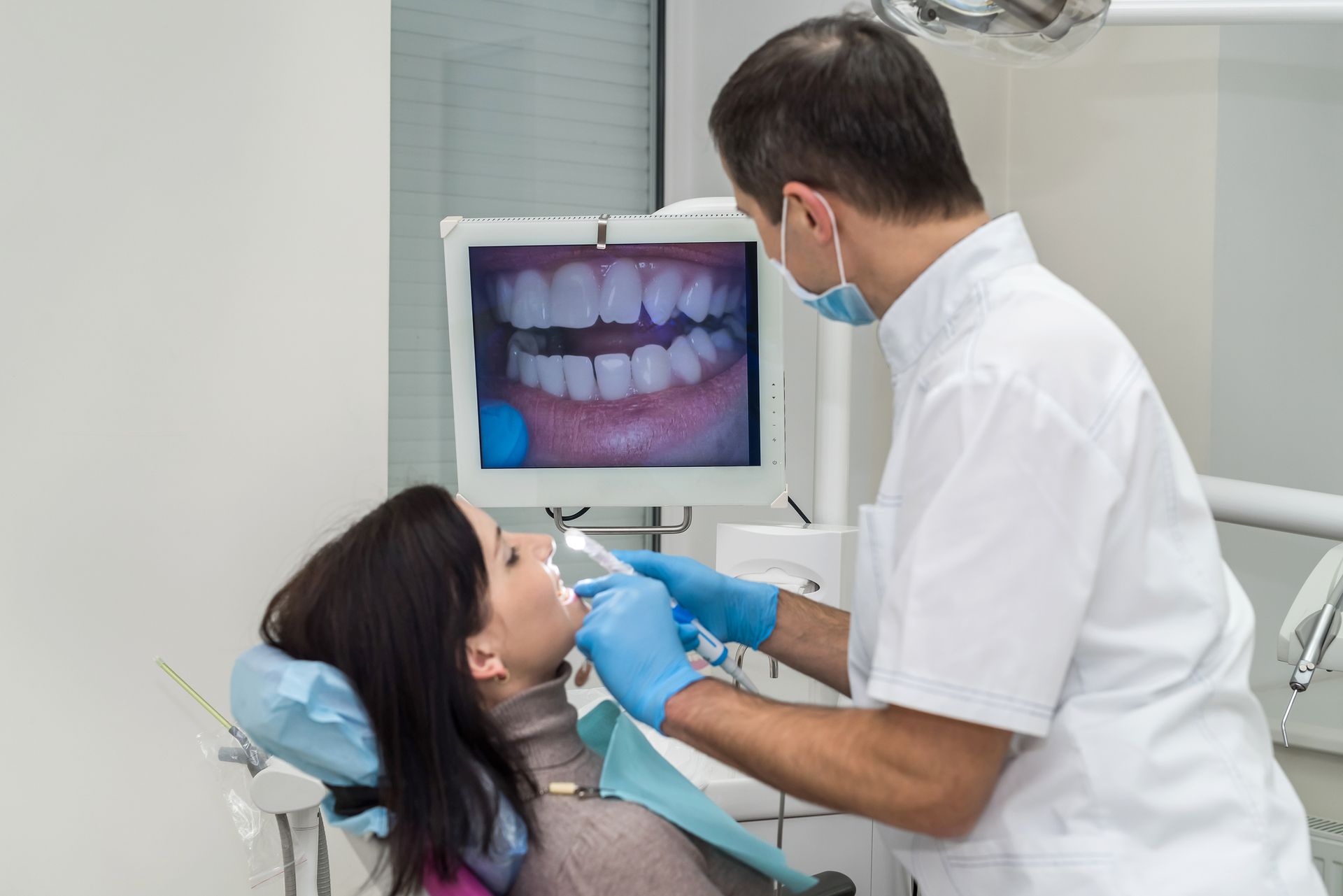 A dentist is examining a woman 's teeth in a dental office.