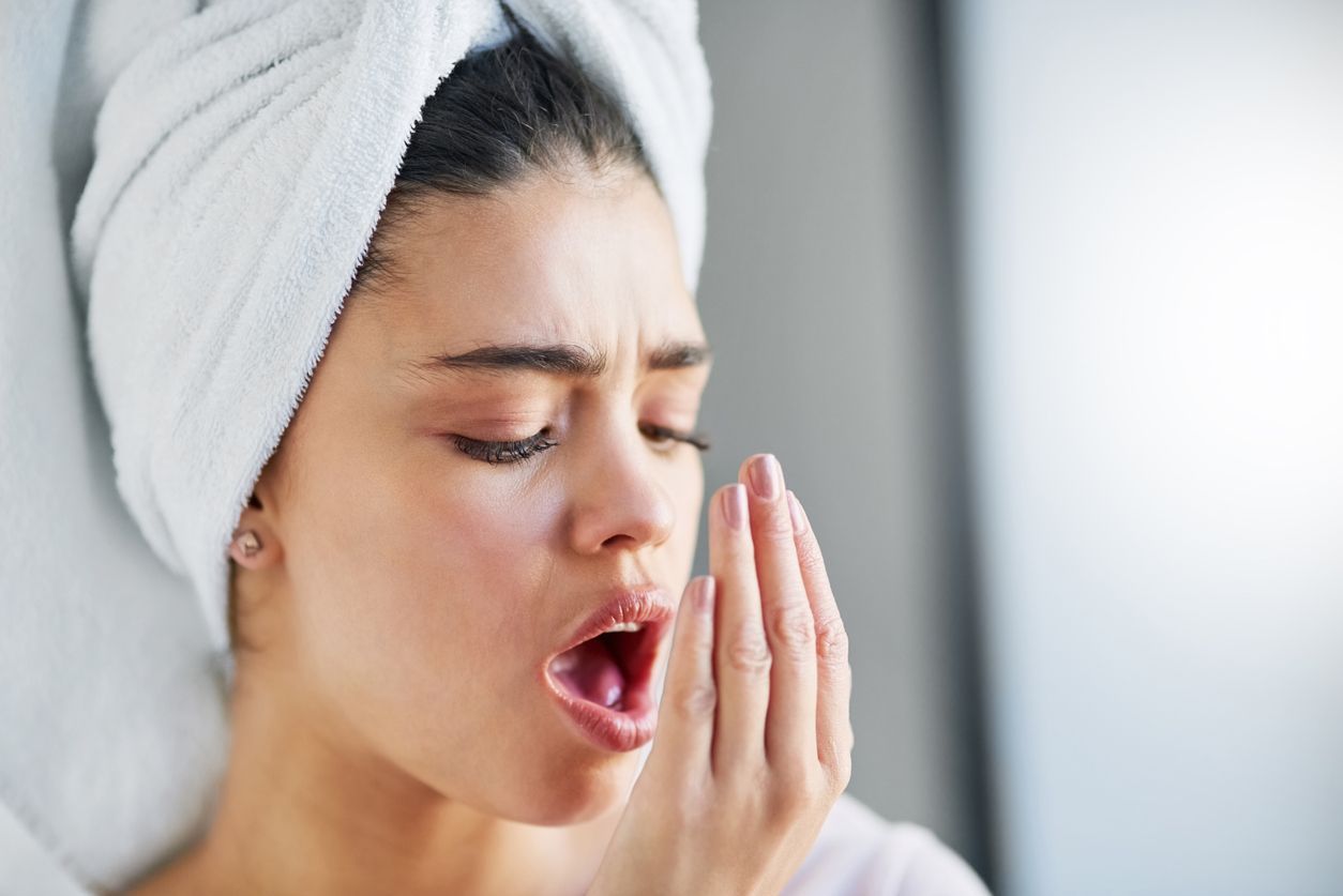 A woman with a towel wrapped around her head is covering her mouth with her hand.