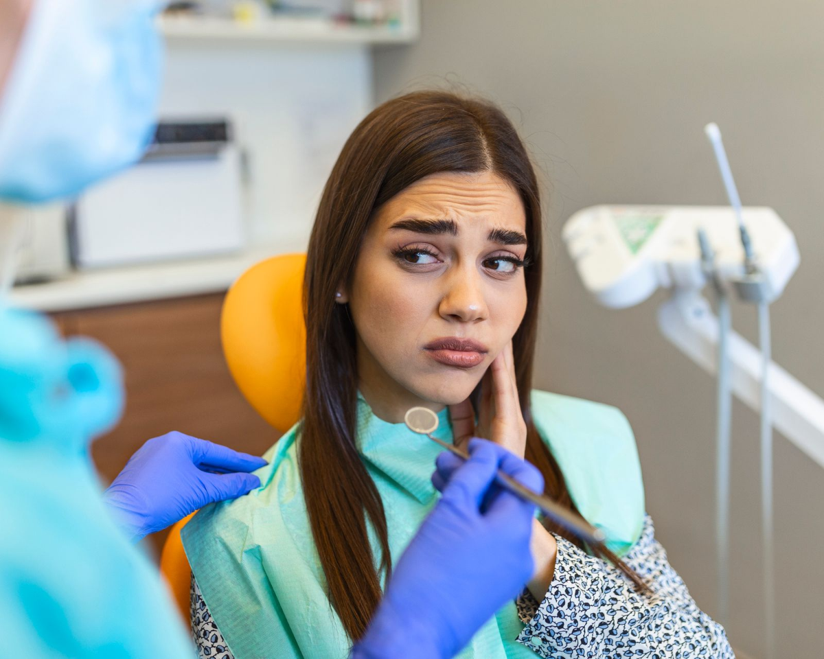Woman with concerned expression in dentist's chair, dentist examining her mouth.