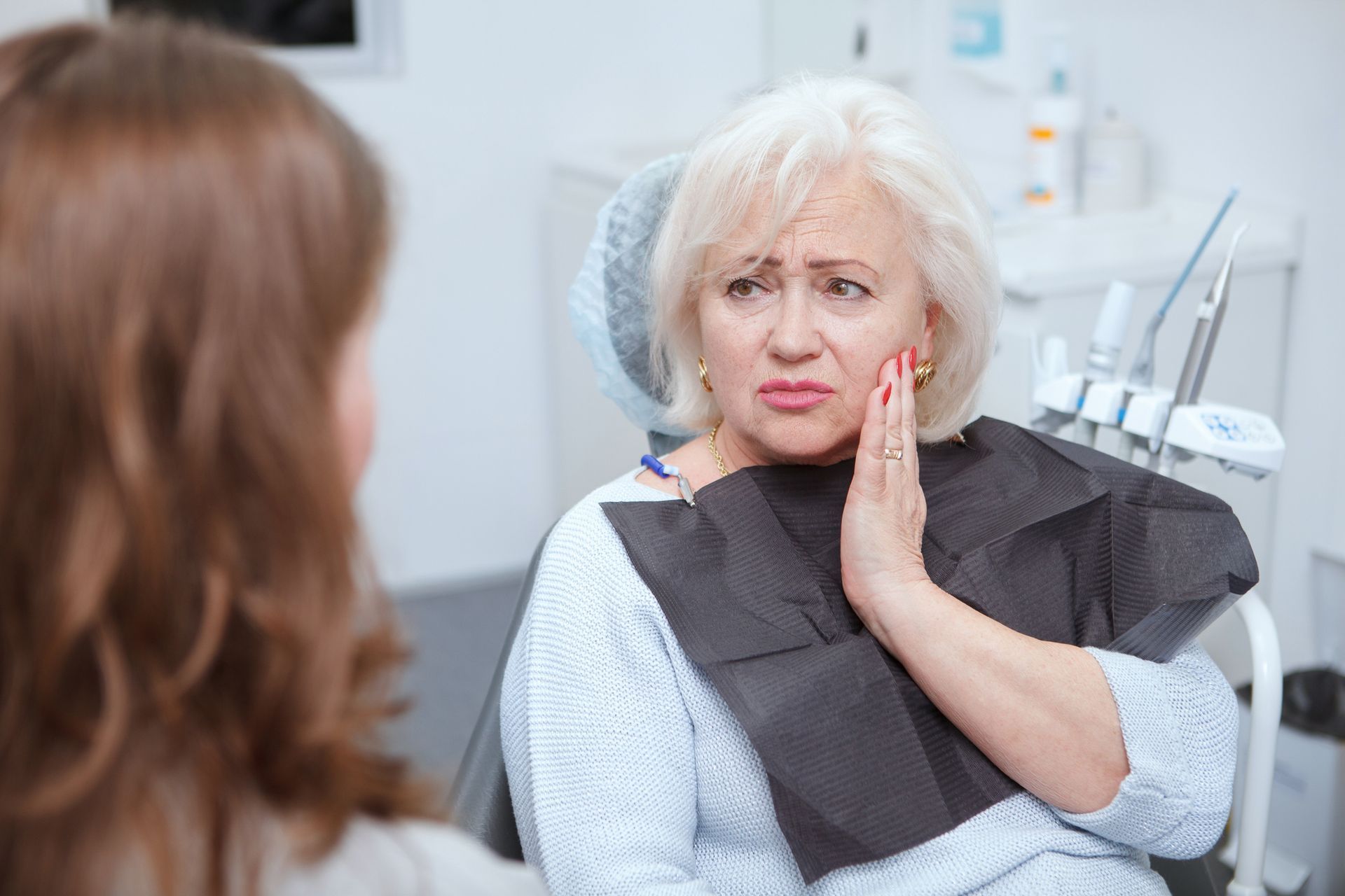 A woman is sitting in a dental chair while a dentist holds a model of a skull.