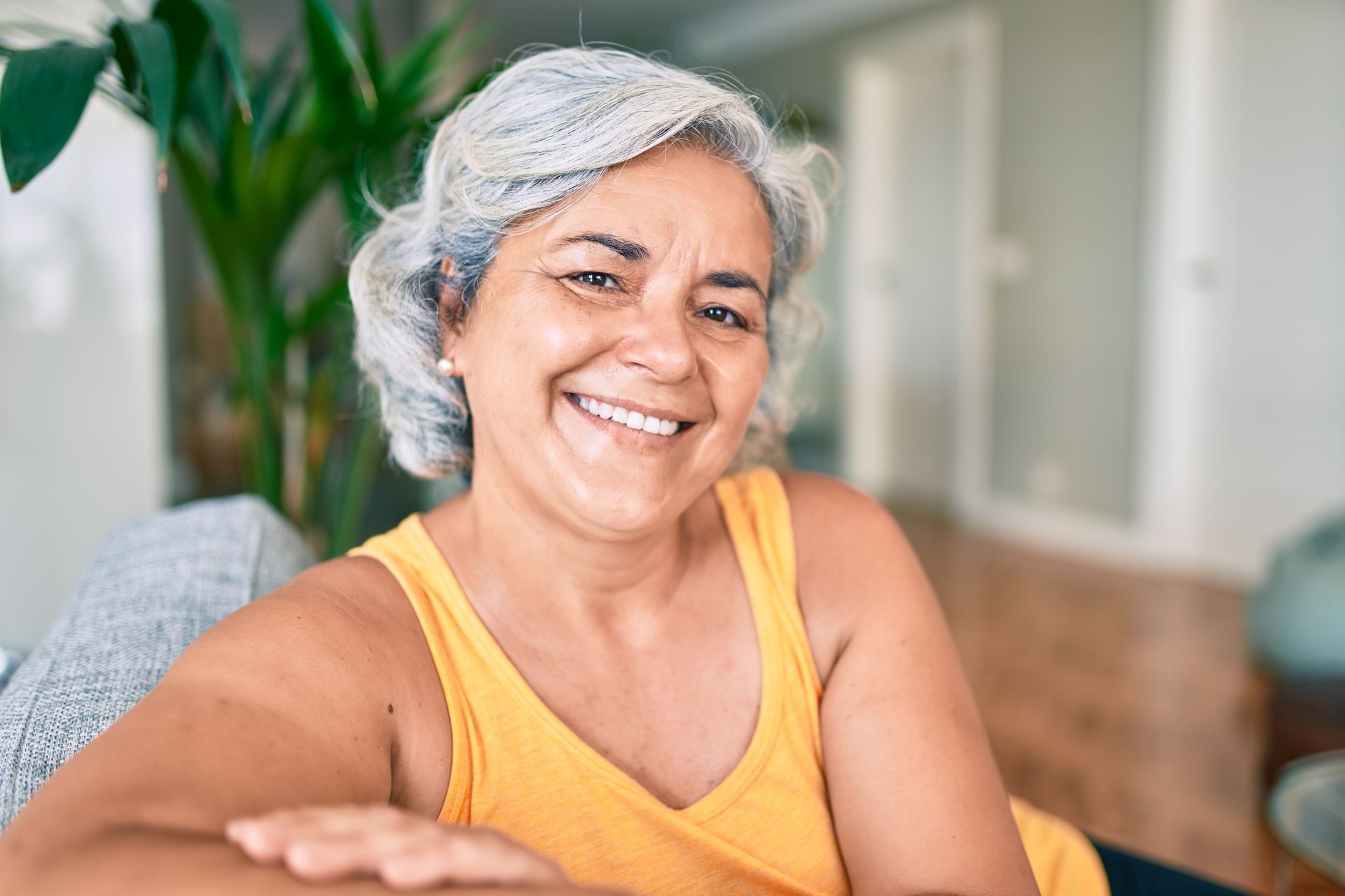 An older woman is smiling while sitting on a couch in a living room.