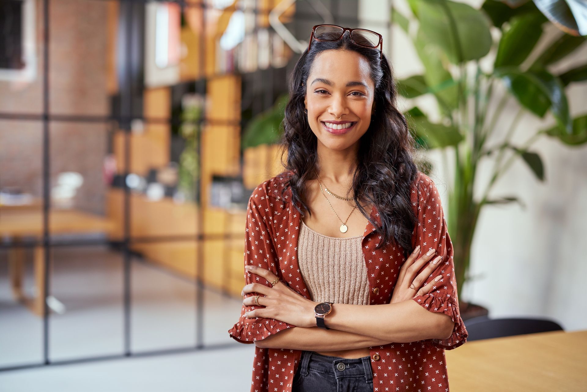 A woman is standing in an office with her arms crossed and smiling.