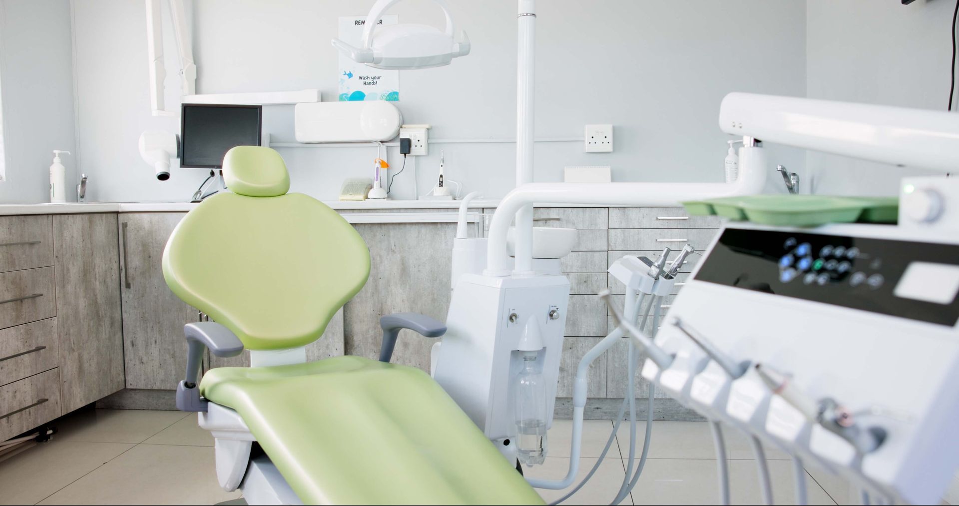 A dental office with a green chair, white equipment, and cabinets.