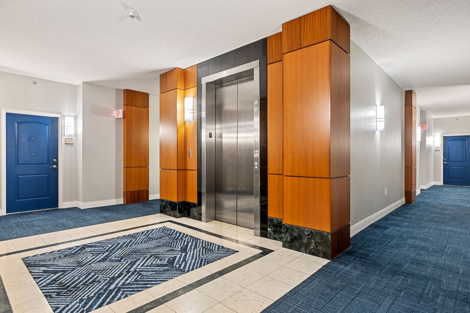 A hallway with a stainless steel elevator and blue doors.