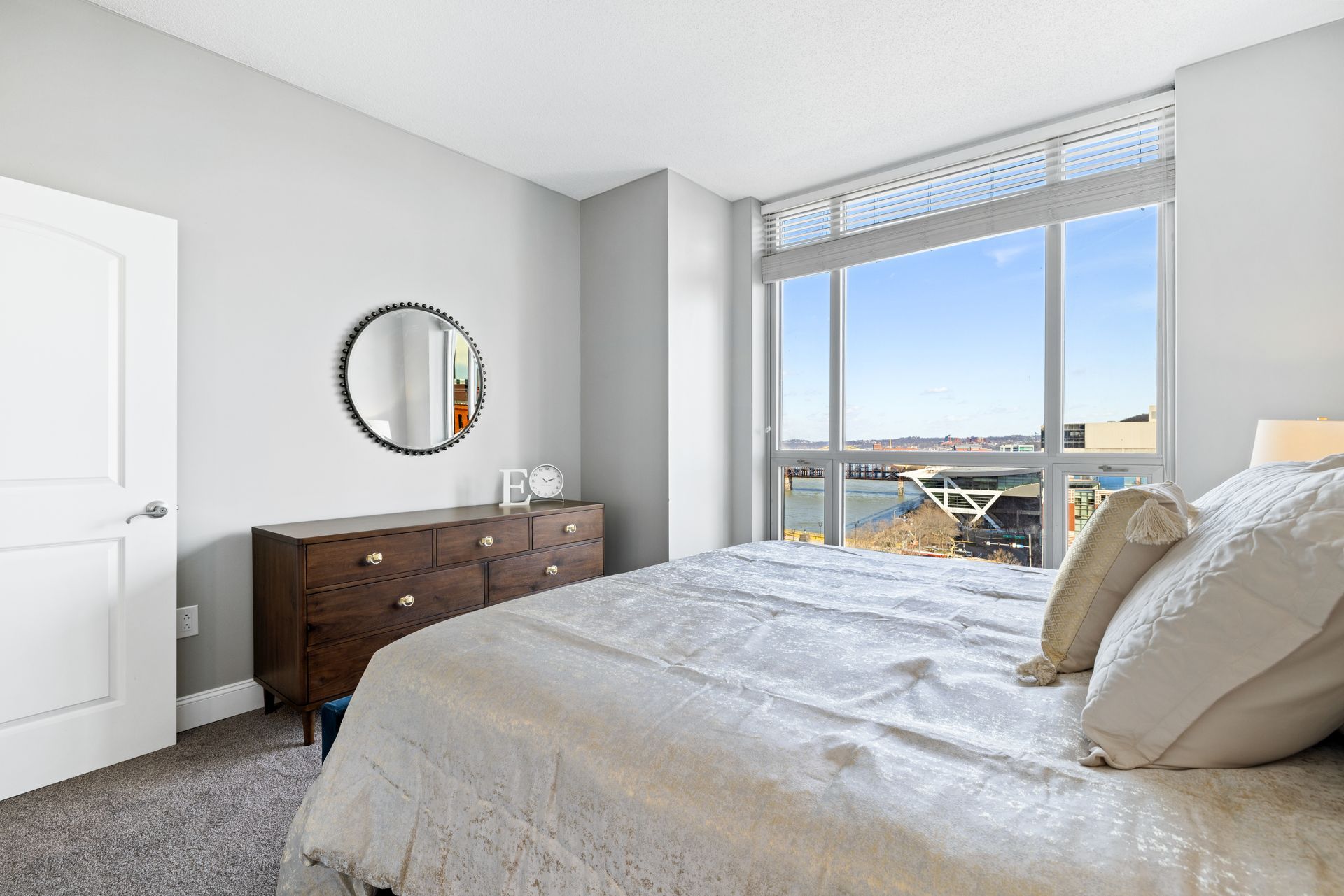 A bedroom with a bed , dresser , mirror and large windows.