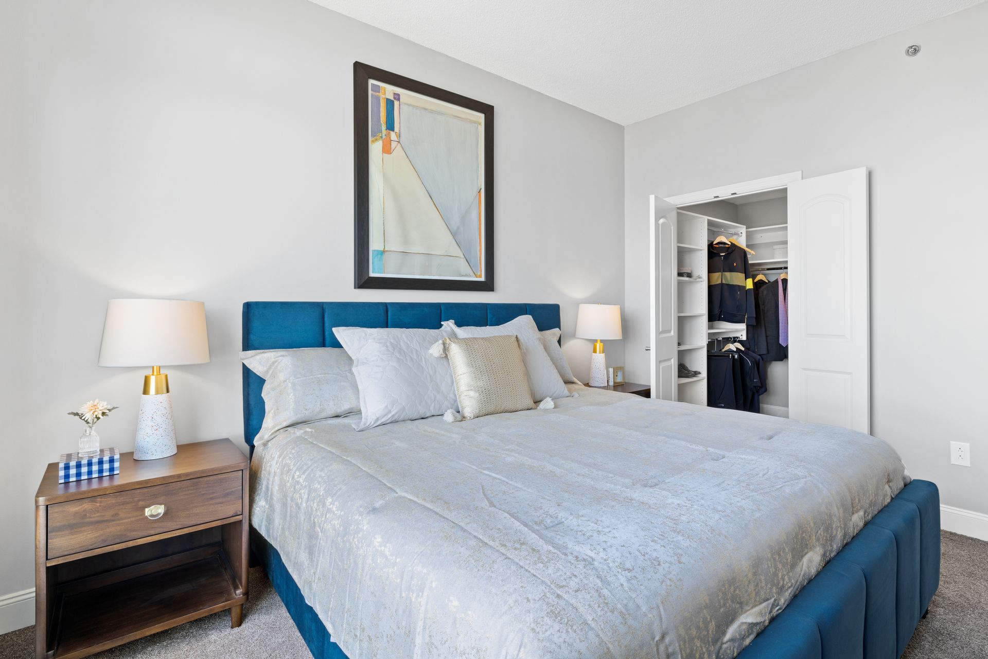 A bedroom with a large bed , nightstand , lamps and a walk in closet.