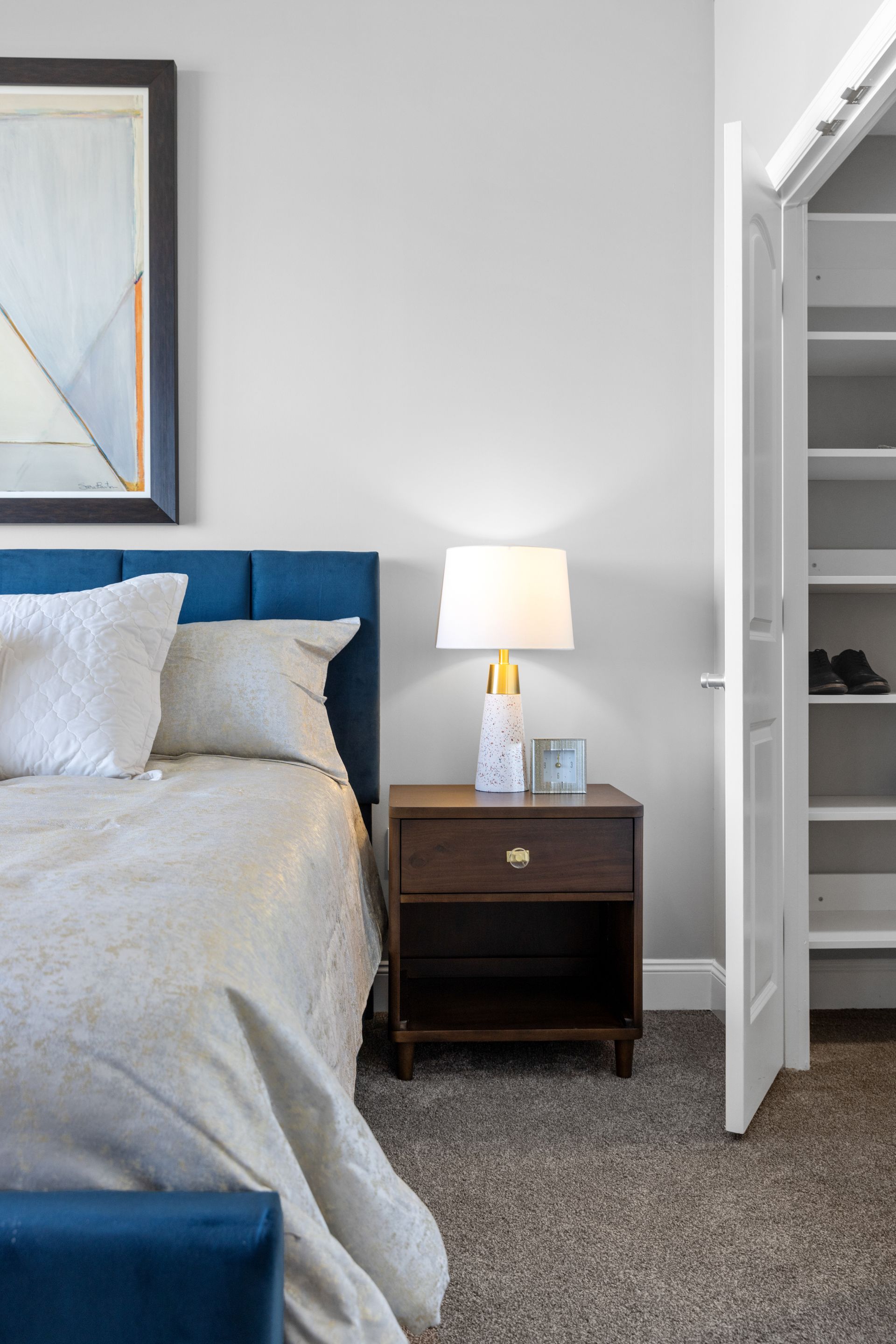 A bedroom with a bed , nightstand , lamp and closet.