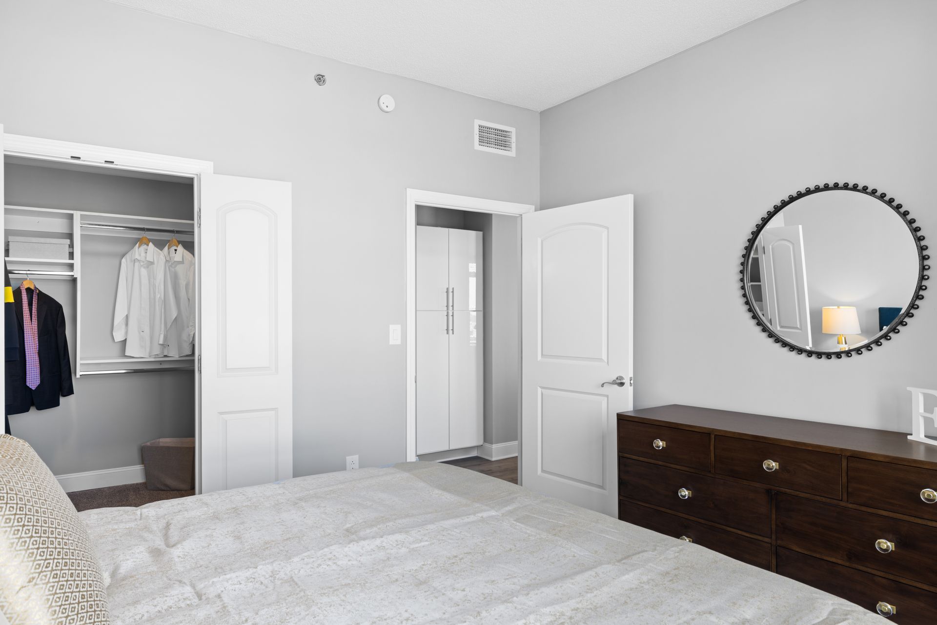A bedroom with a bed , dresser , mirror and walk in closet.