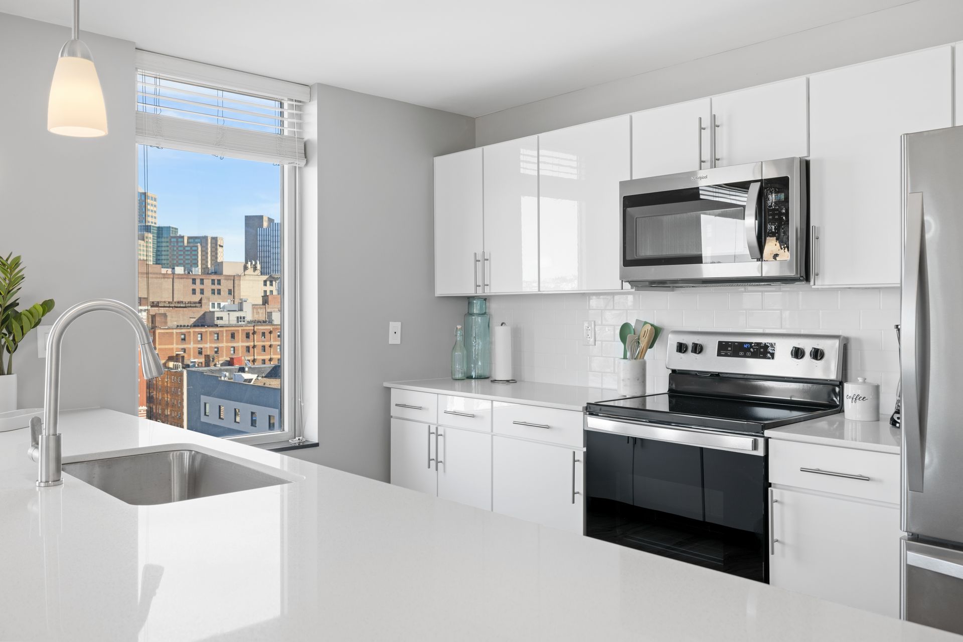 A kitchen with white cabinets , stainless steel appliances , a sink , and a window.