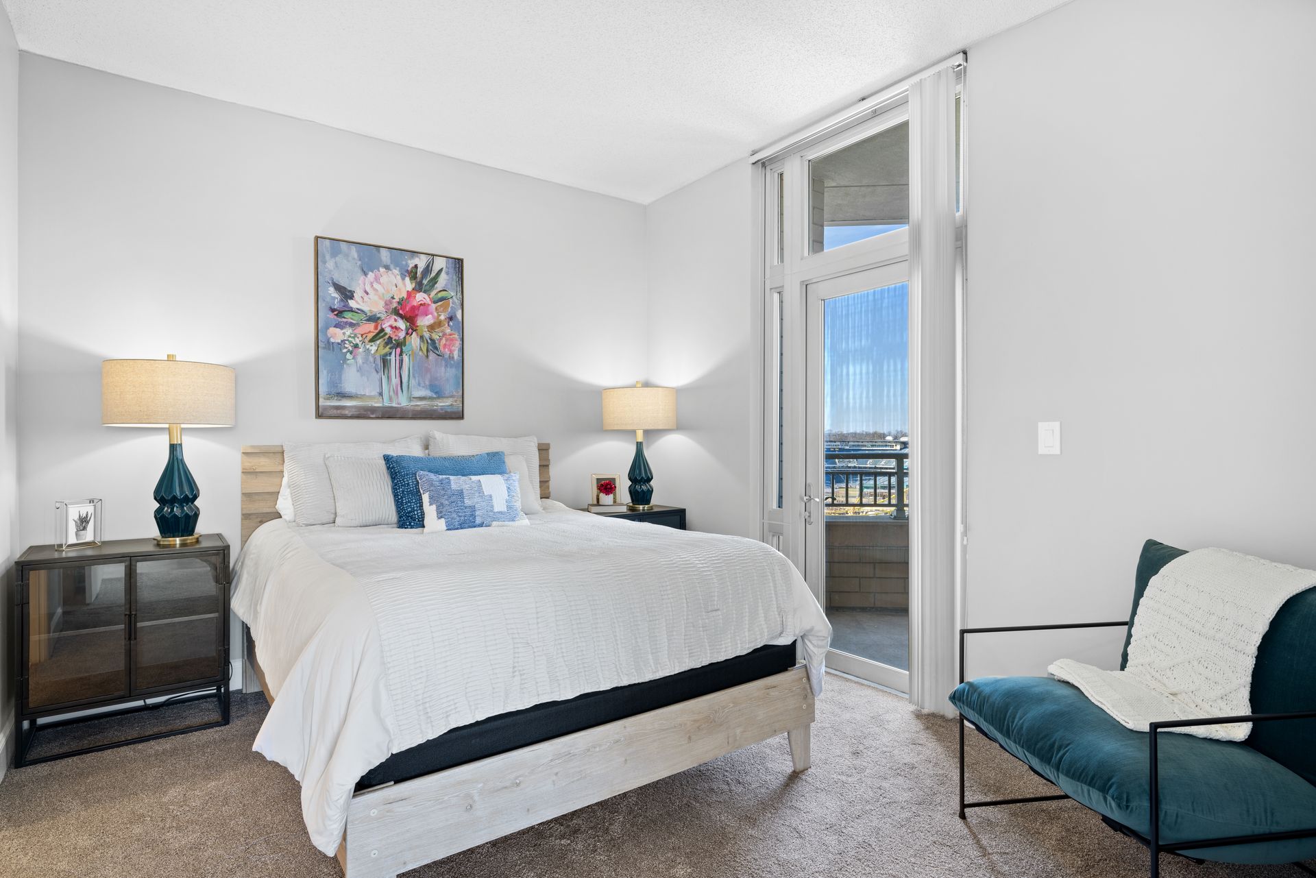 A bedroom with a bed , chair , nightstand , lamps and a balcony.