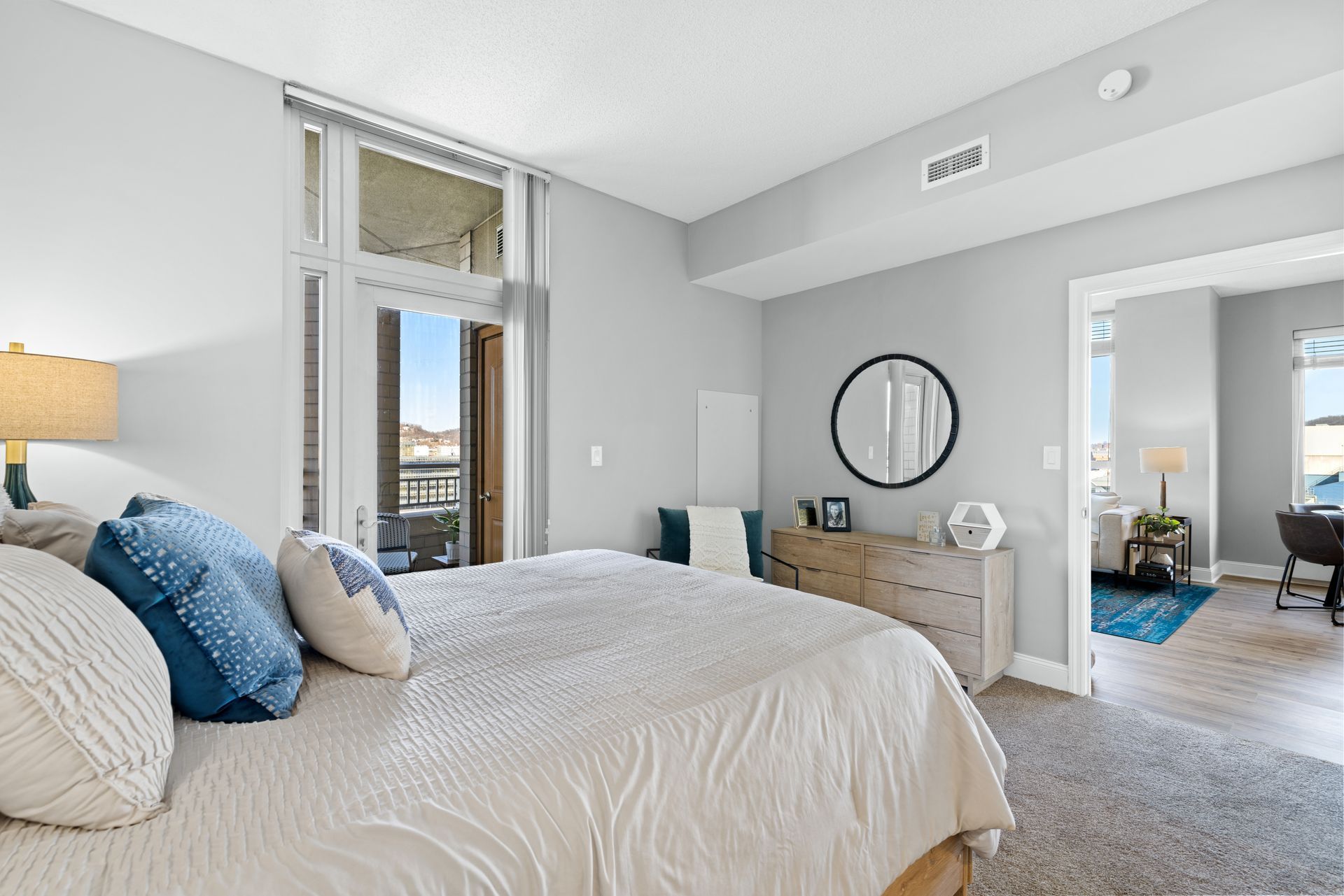 A bedroom with a large bed , dresser , mirror and balcony.