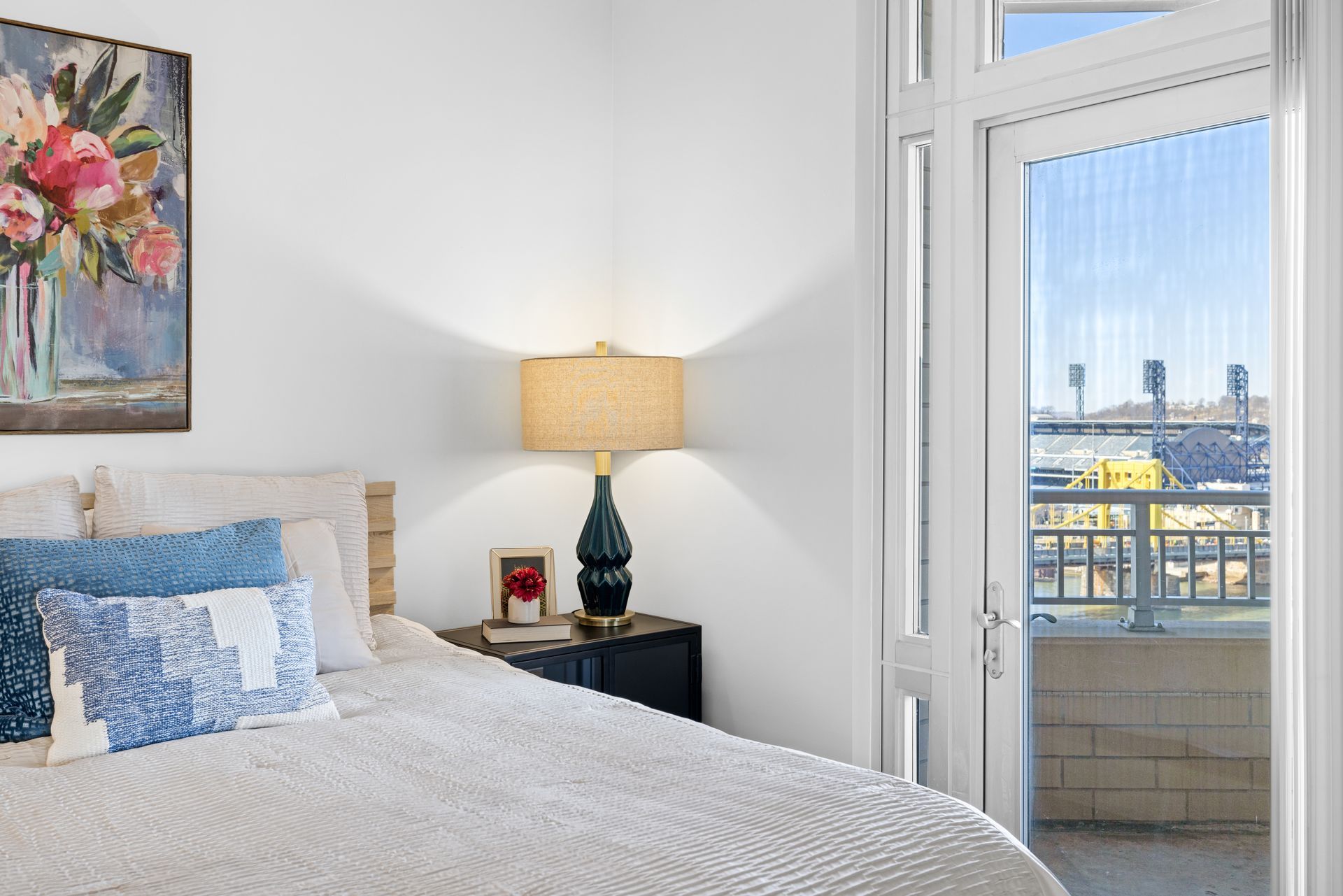 A bedroom with a bed , lamp , nightstand and a balcony.