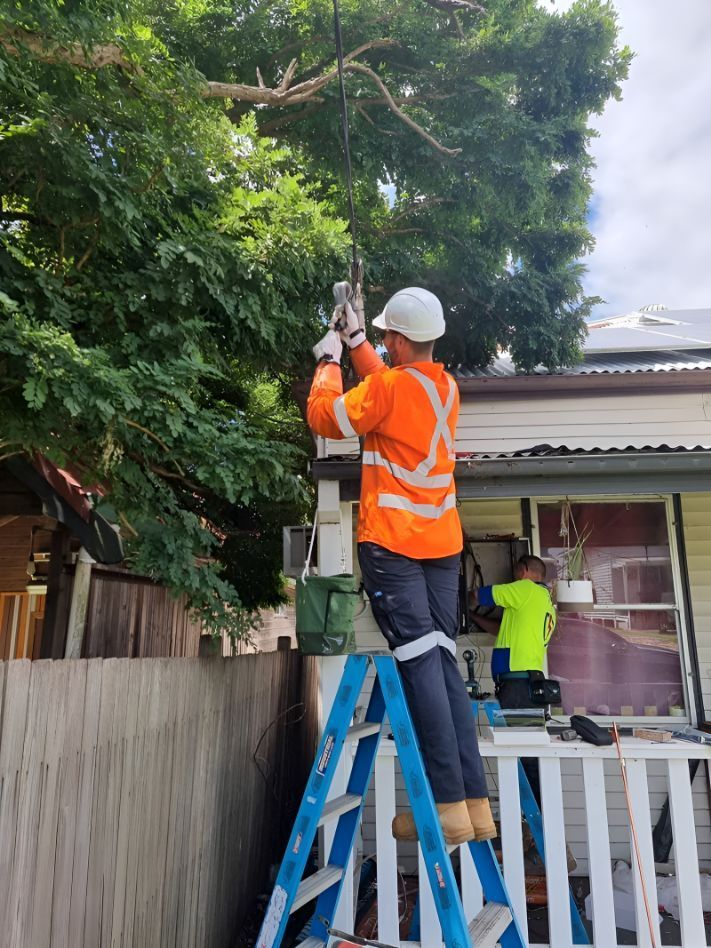 A Man Is Standing On A Ladder In Front Of A House — Entire Power Solutions In Thornton, NSW