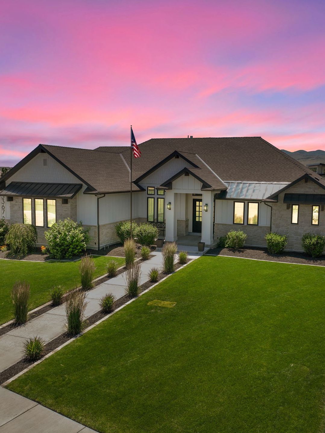 An aerial view of a large house with a lush green lawn and a sunset in the background.