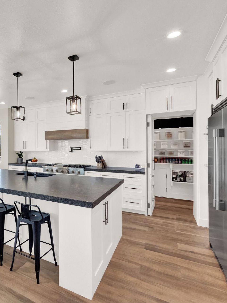 A kitchen with white cabinets , stainless steel appliances , hardwood floors and a large island.