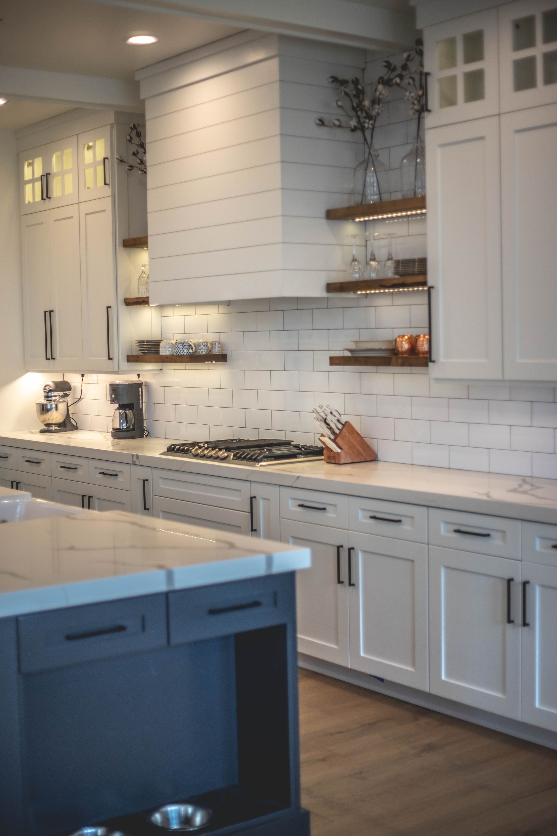 A kitchen with white cabinets , a stove , a sink , and a hood.