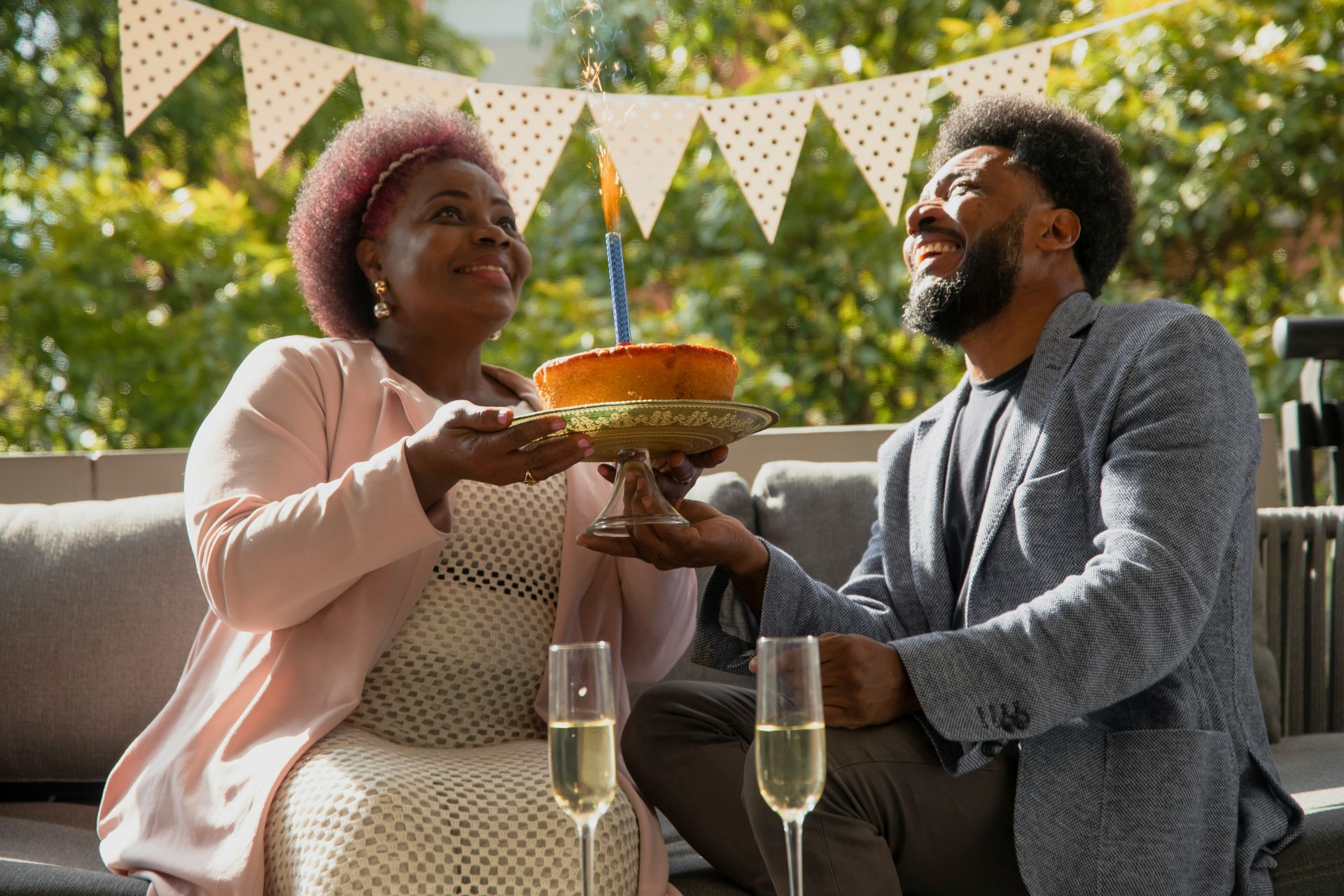 A man and a woman are sitting on a couch holding a birthday cake.
