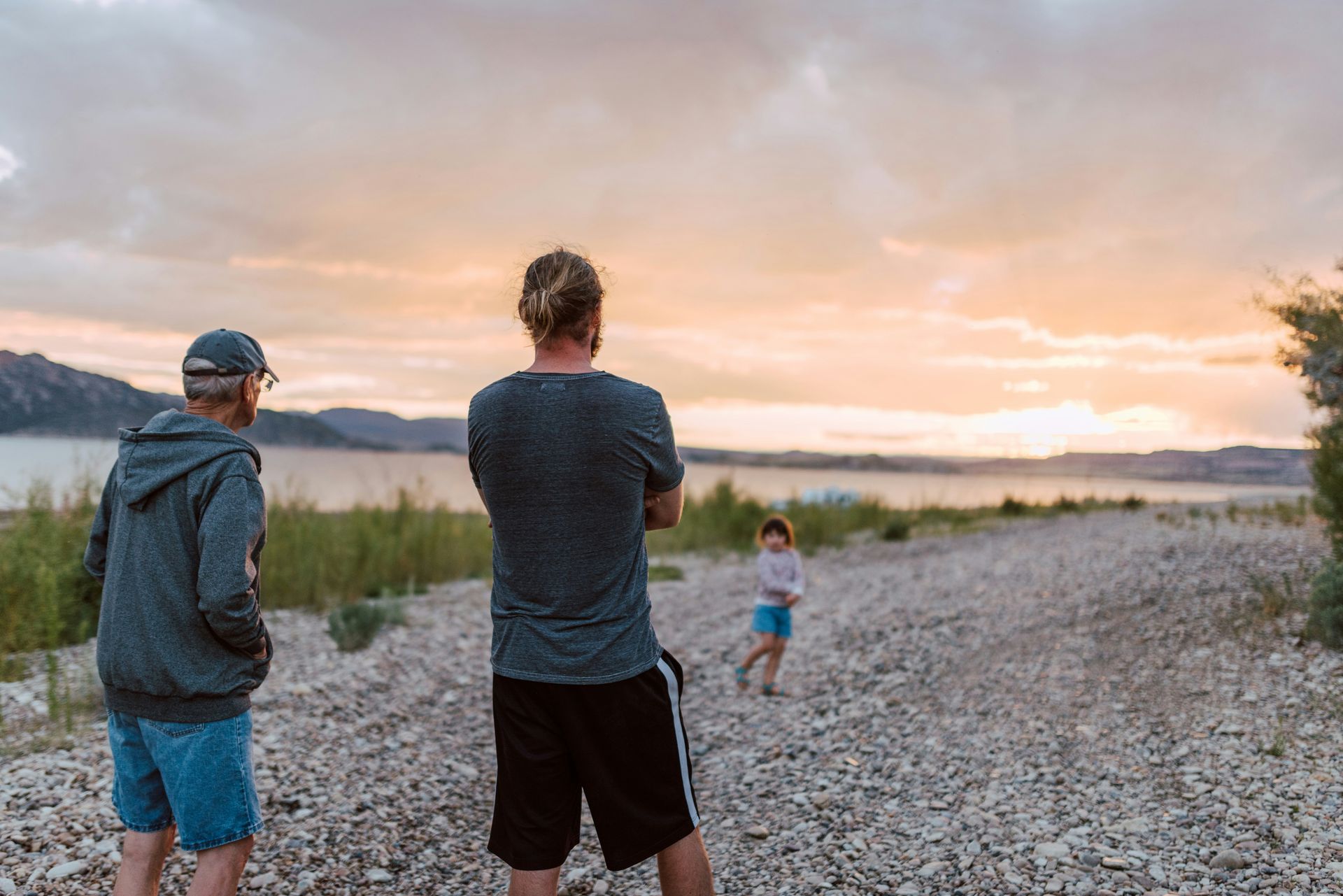 Two men are standing on a rocky beach taking a picture of a little girl.