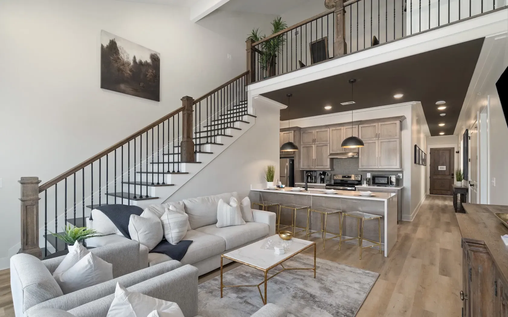 A living room with a staircase leading up to the second floor and a kitchen.