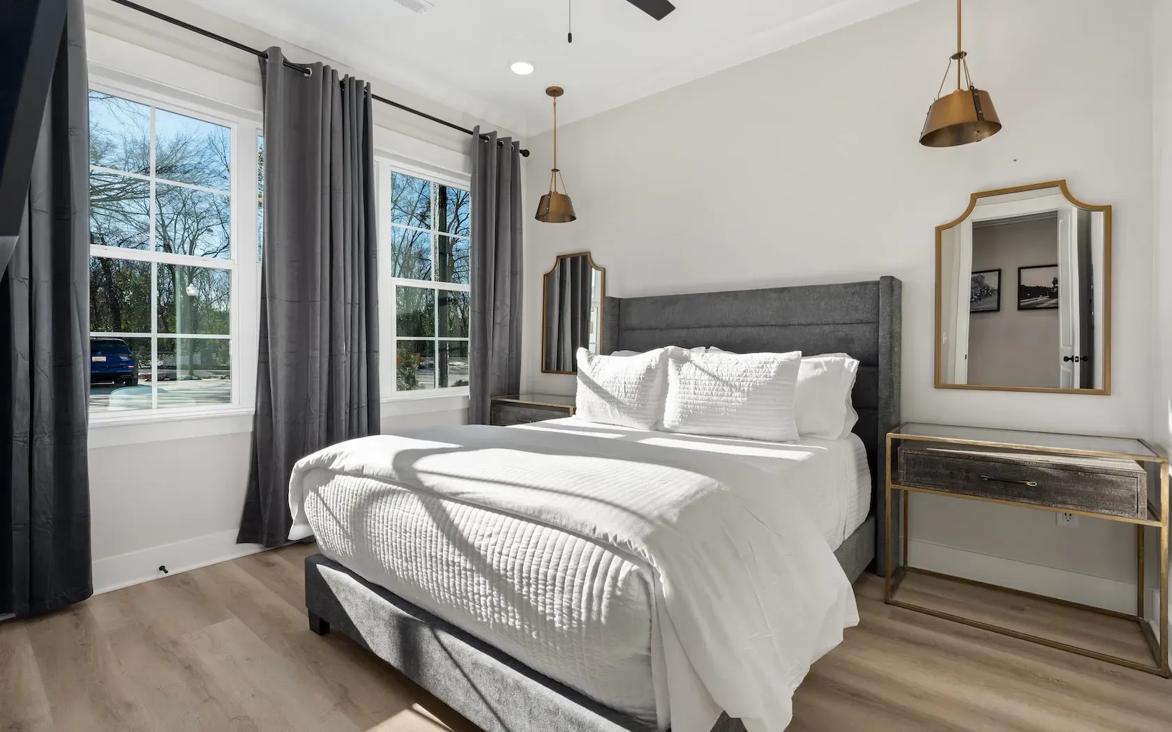 A bedroom with a king size bed , a mirror , and two windows.