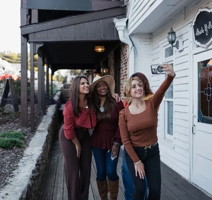 Three women are taking a selfie in front of a building.